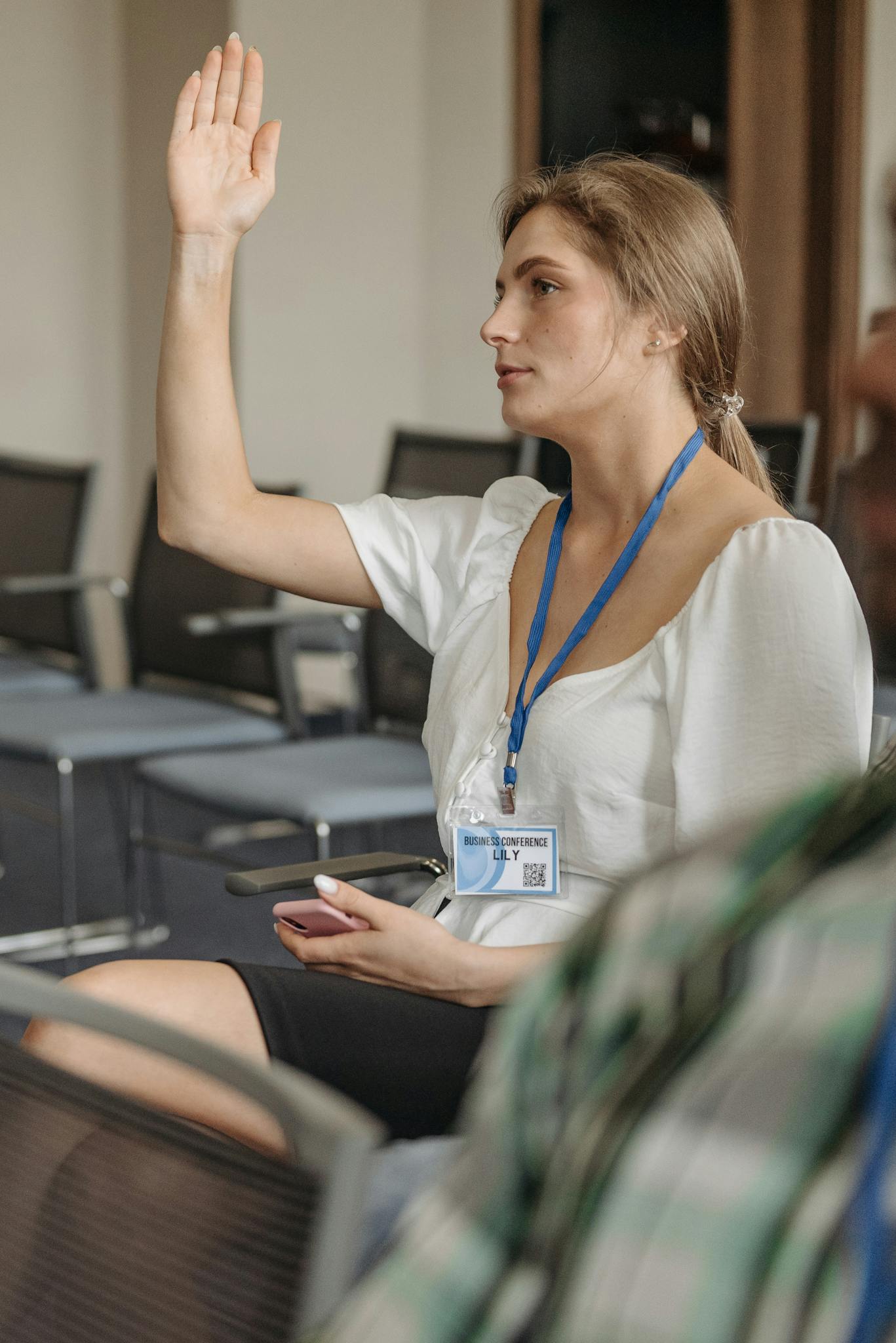 Woman in business attire raising hand at a conference, promoting active participation.